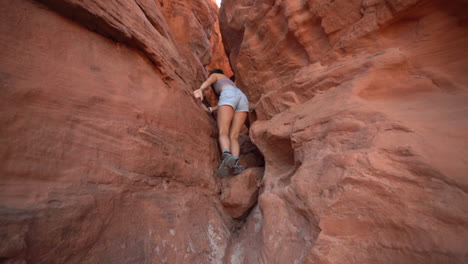 young woman climbing on a red rocks in very narrow eroded slot canyon, valley of fire state park, nevada usa, full frame