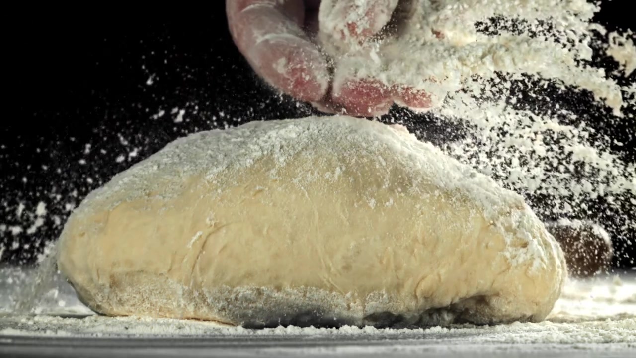 Mano che sparge farina sull'impasto al rallentatore