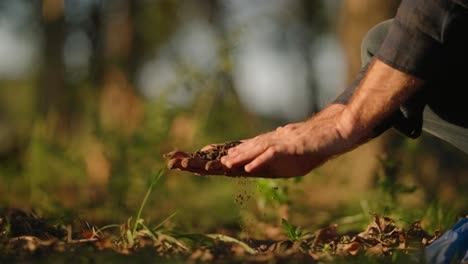 Slow-motion-of-hands-feeling-soil-on-organic-farm,-sifting-through-dirt-at-inspirational-golden-hour