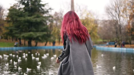 happy smiling woman in warm coat feeding the gulls by the pond in park in autumn. slowmotion shot