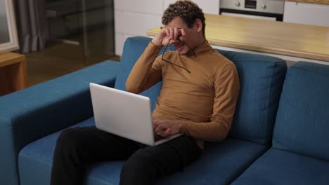 Diverse-ethnic-young-man-using-laptop-on-the-sofa-and-got-tired