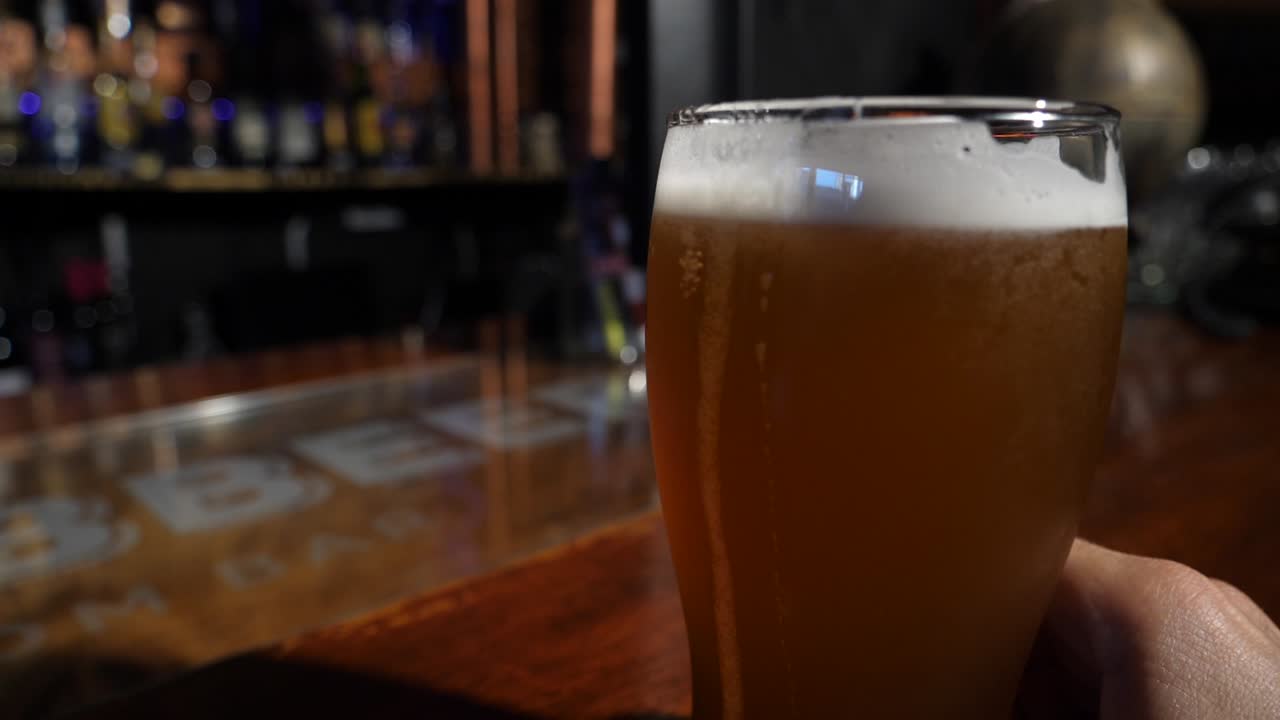 Mano che tiene un bicchiere di birra su un bancone da bar in legno