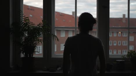 woman standing in front of apartment window in gray, early morning