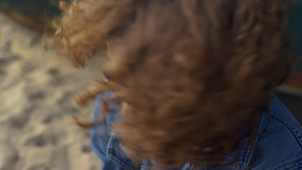 카메라를 보고 있는 소녀가 얼굴에서 곱슬머리를  ⁇ 고 있다. 여자가 곱슬머리를 흔들고 있다.