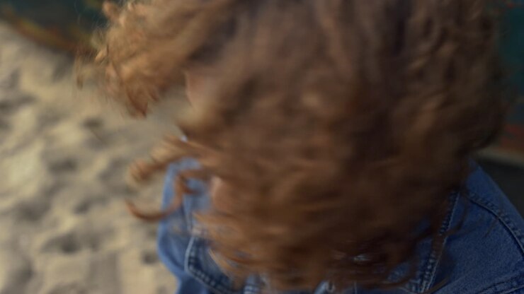 Primo piano di una ragazza che guarda la fotocamera soffiando via i capelli ricci dal viso. Donna che scuote i ricci.