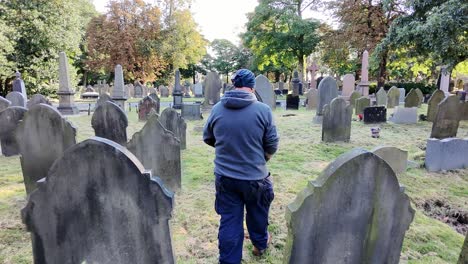 following behind male wearing hat and casual clothing walking alone in peaceful sunlit cemetery