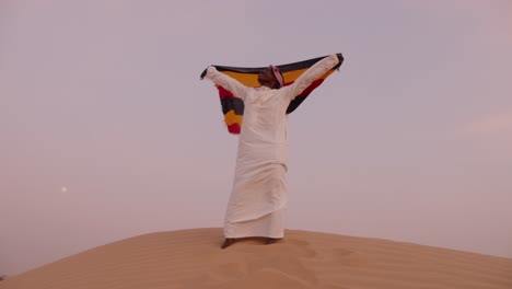 hombre africano levantando la bandera de uganda en el desierto