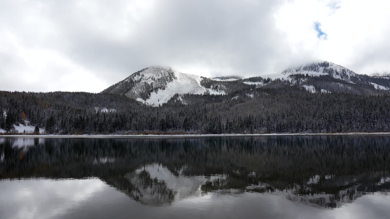 Riflesso a specchio del Lost Lake, nuvoloso e drammatico, al Kebler Pass in Colorado. Pomeriggio freddo e gelido, scontro tra autunno e inverno, con la prima neve bianca e la foresta di pioppi tremuli rossi, gialli e arancioni nelle Montagne Rocciose.
