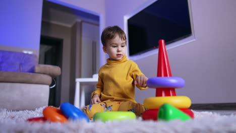 cute calm little boy playing with pyramid. kid sits on the floor assembling a toy. low angle view.
