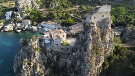 aerial flyover beautiful of old historic village scopello with ocean shore,cliffs and old buildings during sunny day in italy