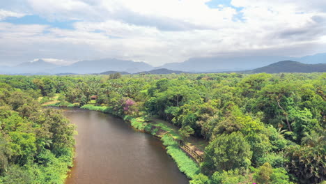 drone shot going up revealing a beautiful scenery river in tropical green forest with mountains in background