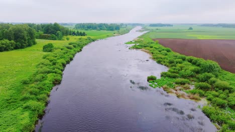 cinematic drone tracks river curve through rural latvia under cloudy skies