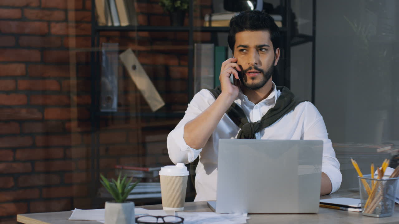 Stylish Arabian Businessman Sitting At His Desk With Laptop In The Office And Talking On The Phone, Then Gets Up And Walks Away