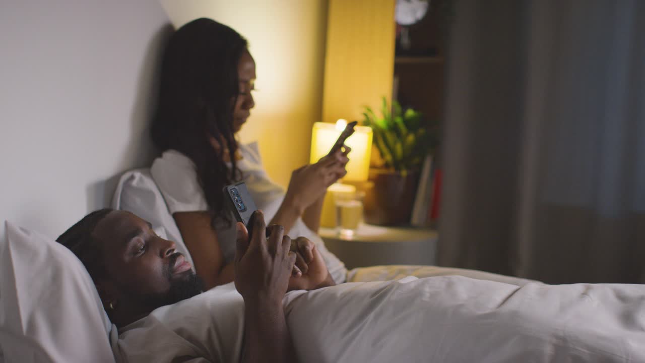 Couple With Relationship Problems At Home At Night Both Looking At Mobile Phones In Bedroom 11