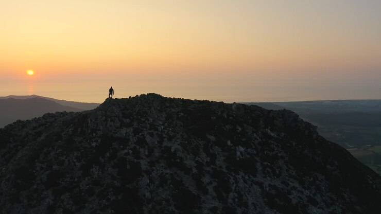 Ripresa aerea - Sorvolando l'uomo da davanti a dietro, in piedi sulla cima della montagna, che ammira uno splendido tramonto o alba sulle vette.