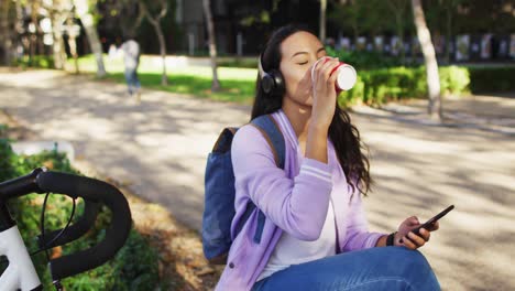 asian woman wearing headphones listening to music and drinking takeaway coffee