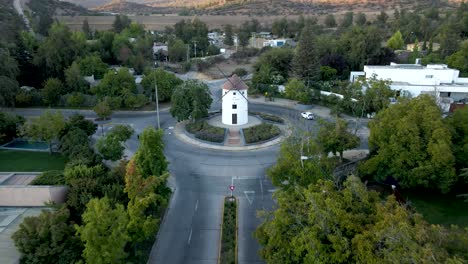 aerial dolly out of leonidas montes windmill in roundabout with cars driving surrounded by trees, hills in background, lo barnechea, santiago, chile