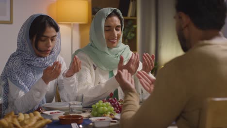 Muslim-Muslim-Family-Sitting-Around-Table-At-Home-Saying-Prayer-Before-Meal