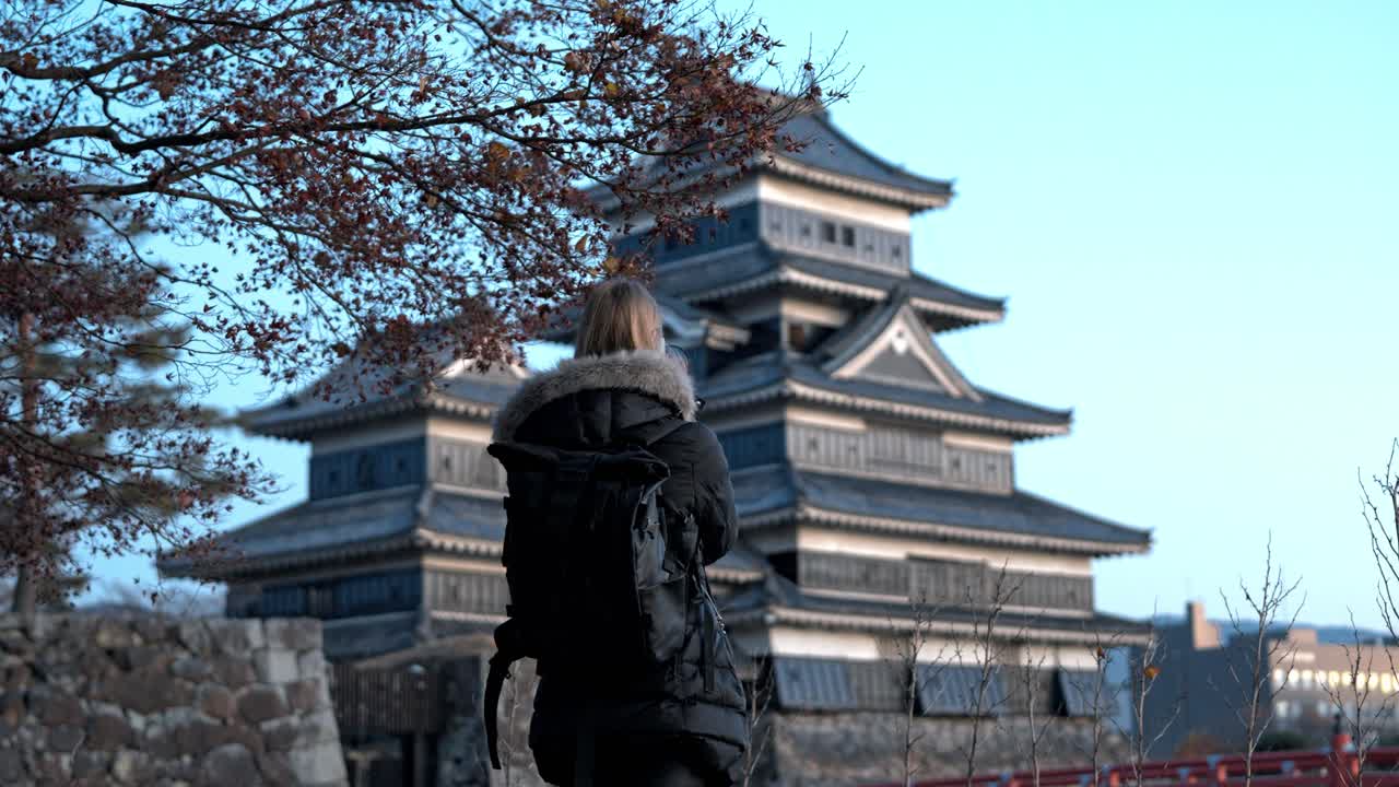 A cinematic clip of a girl photographing the stunning Matsumoto Castle in autumn, framed by colorful fall foliage.