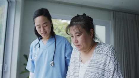 smiling asian female doctor helping happy female patient walk with walking frame at hospital