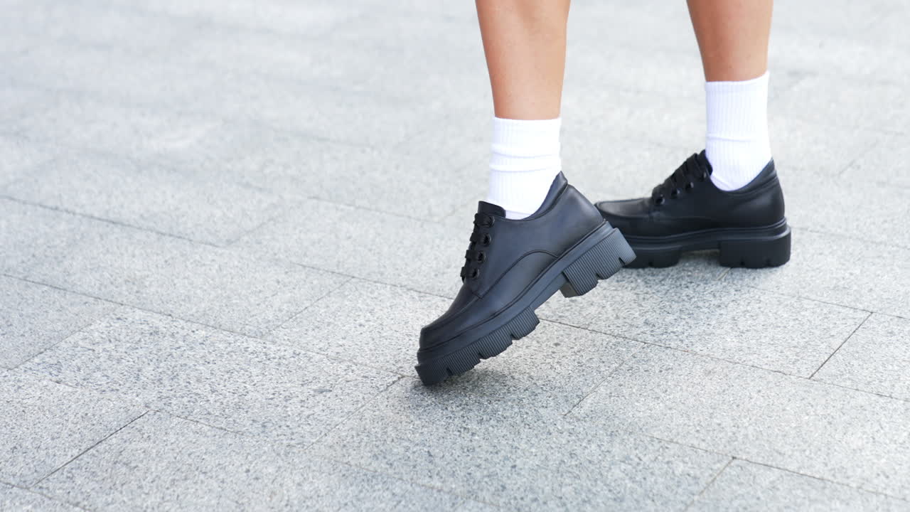 Fashionable shoes demonstration. Model in white socks wears black leather oxford boots on tractor soles with thick laces. High angle view.
