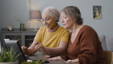 arabic woman teaching an elderly woman to use a laptop at home