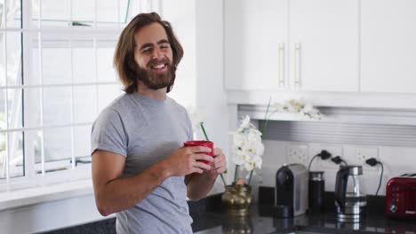 Retrato-De-Un-Hombre-Caucásico-Sosteniendo-Una-Taza-De-Café-Y-Sonriendo-En-La-Cocina-De-Casa