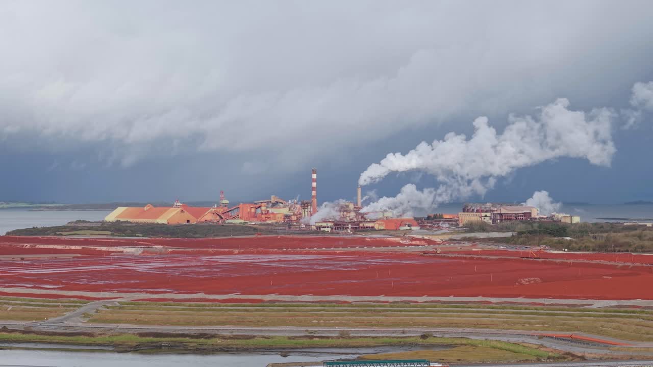 Smoke Coming Out On Chimney Of Alumina Refinery With Bauxite Residue Red Field in The Foreground. - aerial shot