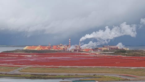 smoke coming out on chimney of alumina refinery with bauxite residue red field in the foreground. - aerial shot
