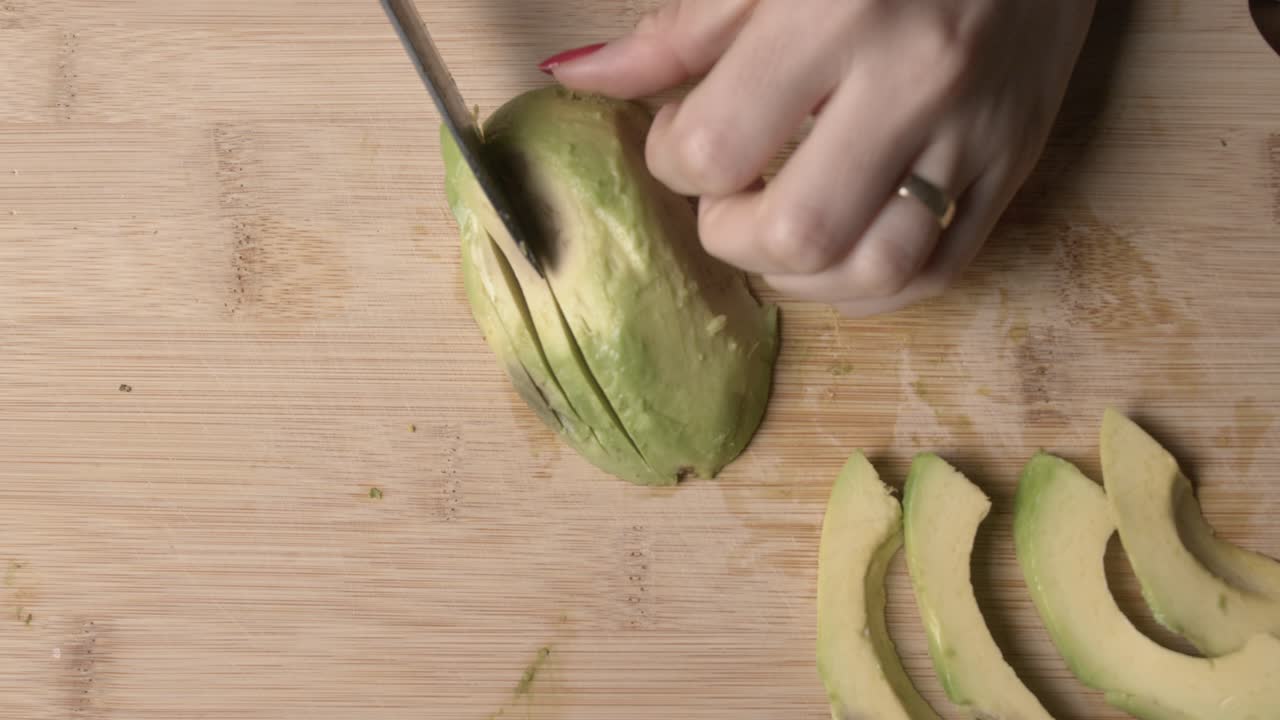 A close-up of a woman slicing a ripe avocado on a wooden chopping board