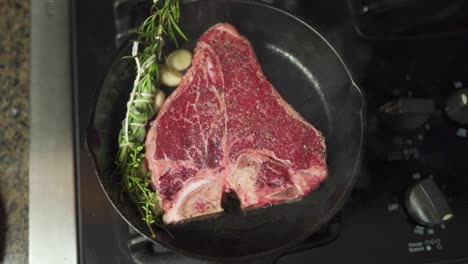slo-mo footage moving over a juicy steak, garnished in herbs and spices, slowly cooking in a cast iron pan on top of an oven range.