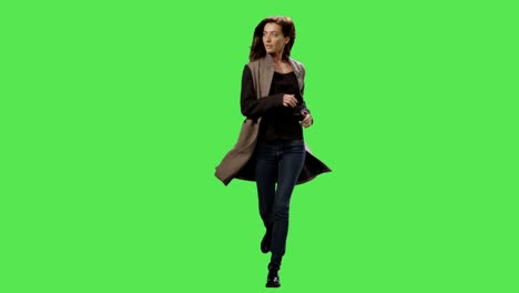 casual brunette female in a coat is running on a mock-up green screen in the background.