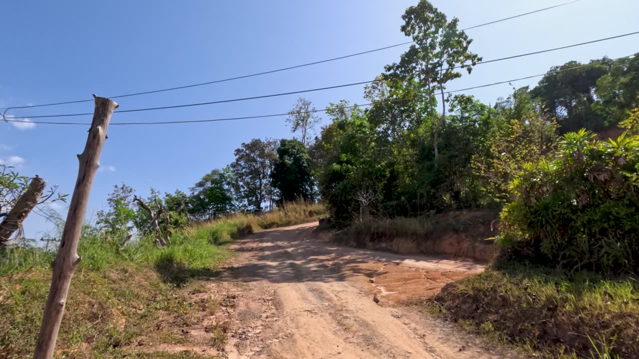 Camera pans from warning sign to uphill dirt road in bright daylight, rural Phuket, Thailand