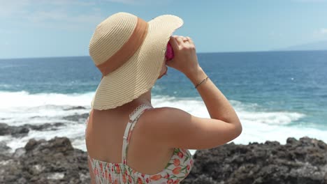 Woman-on-vacation-with-summer-hat-enjoys-fresh-can-beverage-by-sea,-rear