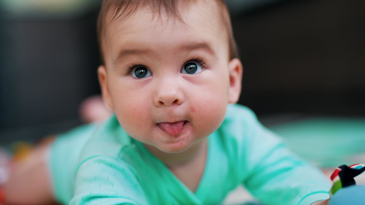 Dear baby boy wearing blue clothes lies on belly. Portrait of a nice active child showing tongue. Close up.