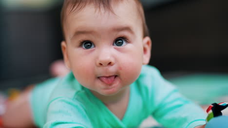 dear baby boy wearing blue clothes lies on belly. portrait of a nice active child showing tongue. close up.