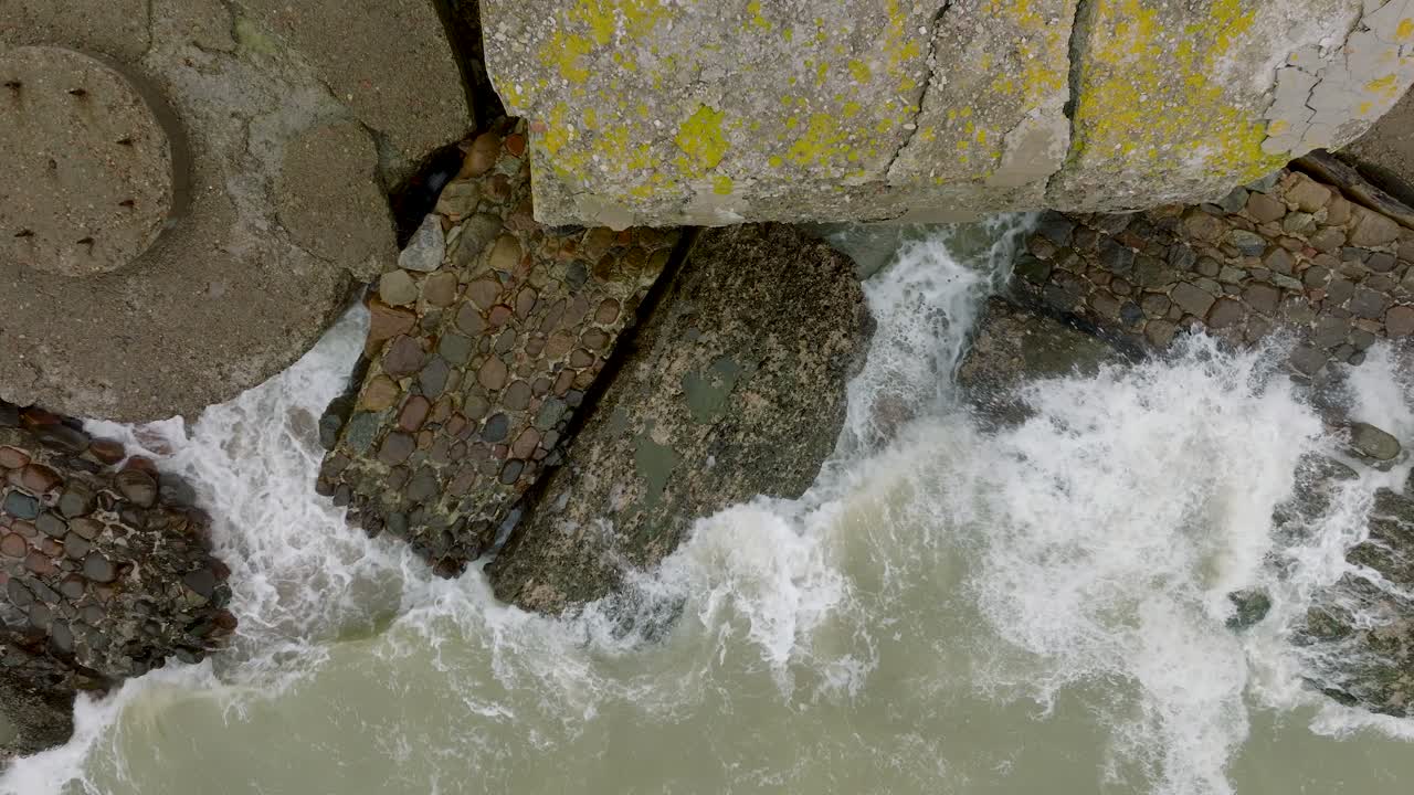 Aerial birdseye view of abandoned seaside fortification buildings at Karosta Northern Forts, Baltic sea coast , large waves, overcast day, slow motion, ascending drone reveal shot
