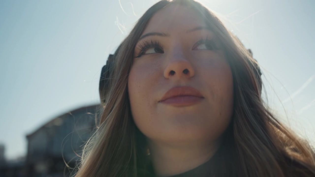 Sunlit redbrick street portrait of woman pointing and gesturing, headphones and coat, expressive profile and candid closeups editorial vibe, empowered and playful mood, warm highlights and crisp