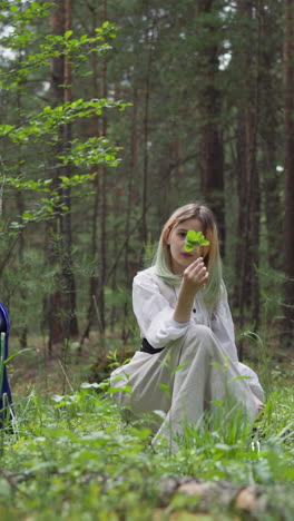 teenage girl looks at green sprout picking herbs with friends on forest glade. medieval magician with students in wild wood. mystical ritual