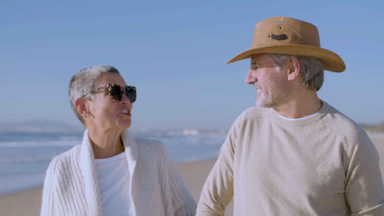 Front view of a happy senior Caucasian couple talking and laughing together while walking on the beach
