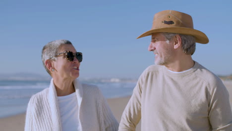 vista frontal de una feliz pareja caucásica hablando y riendo juntos mientras caminan por la playa