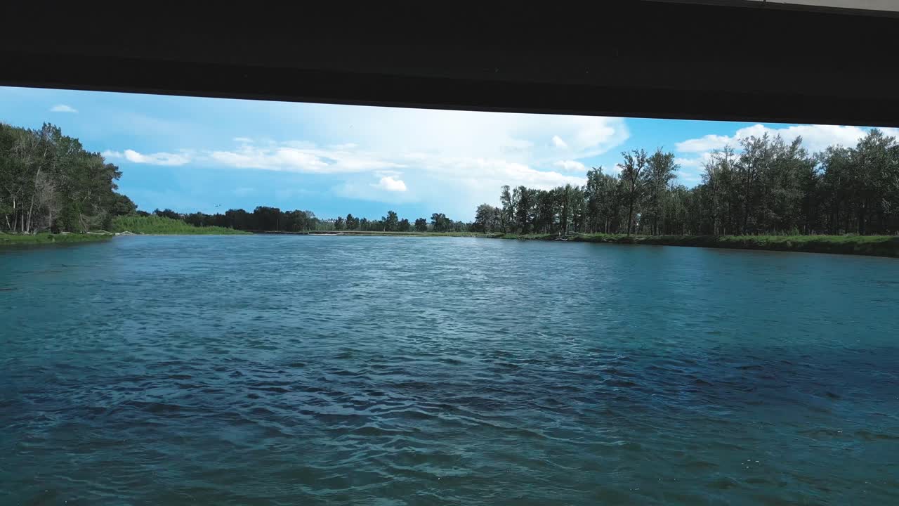 A concrete bridge stretches over a wide river with rippling blue water and cloud-filled skies above