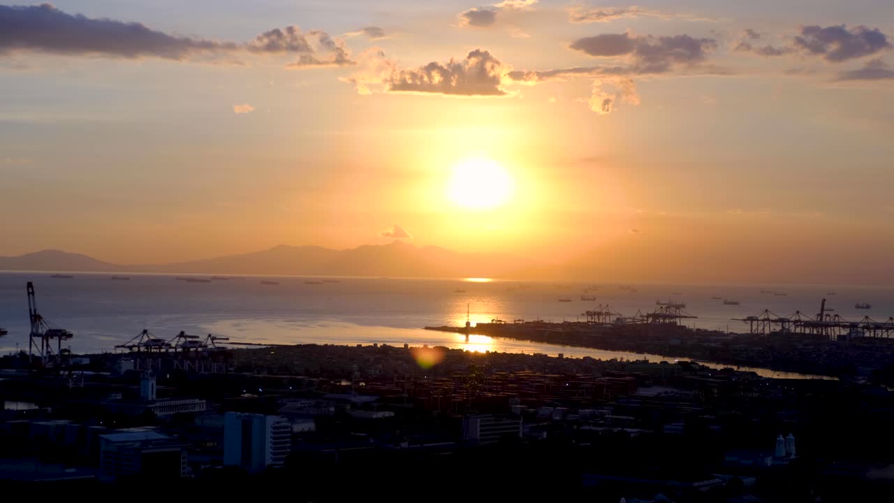 Static aerial ocean view overlooking industrial port with cranes during golden orange sunset in capital city of Manila Philippines
