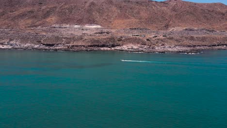 Speedboat-races-along-coast-of-Baja-Mexico-over-turquoise-green-clear-water-on-rocky-coast-to-land-on-sandy-beach