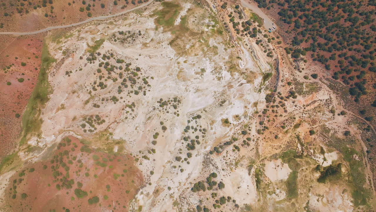 Lifeless dry landscape with some bushes growing on. Road with few cars parked. Aerial view of Travertine, California, USA.