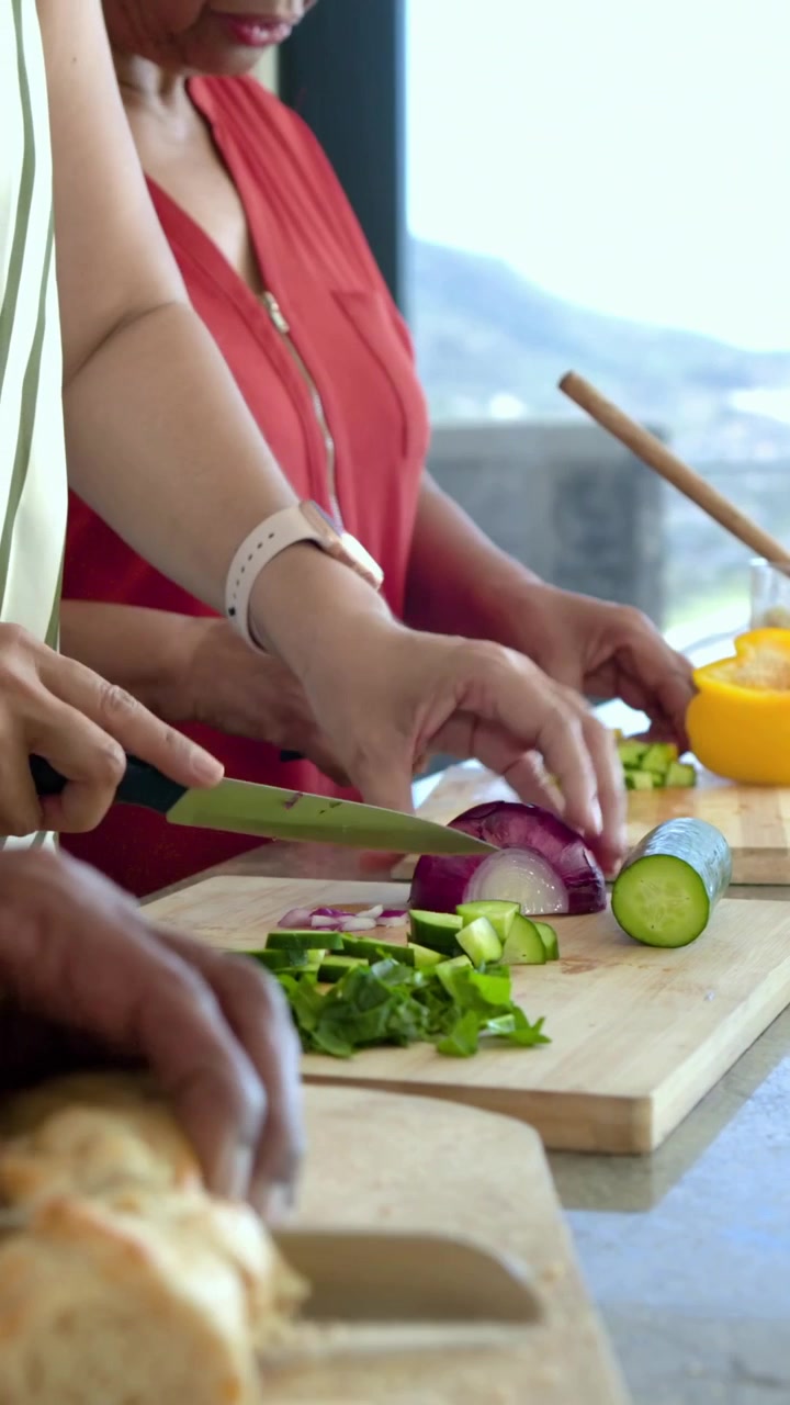 Video verticale: Clip che mostra tre donne, una con un top rosso, che preparano un pasto in cucina tagliando con i coltelli