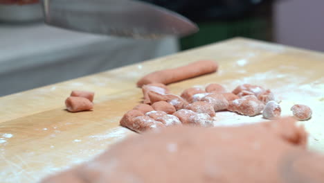 Manos-Que-Agarran-Un-Cuchillo-Que-Corta-Pequeños-Trozos-De-Pasta-En-Una-Mesa-De-Madera