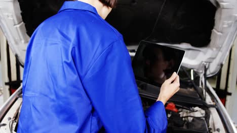 mecánica femenina usando una tableta digital mientras revisa un coche
