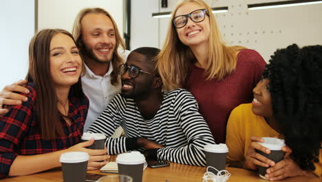 grupo multiétnico de amigos sonriendo y mirando la cámara sentados en una mesa en un café