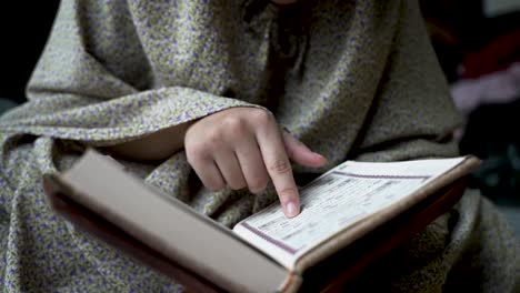 sentado en el suelo en medio de una pila de ropa, un individuo lee un libro religioso en una secuencia de cámara lenta, simbolizando la búsqueda de estudio y aprendizaje en el hogar